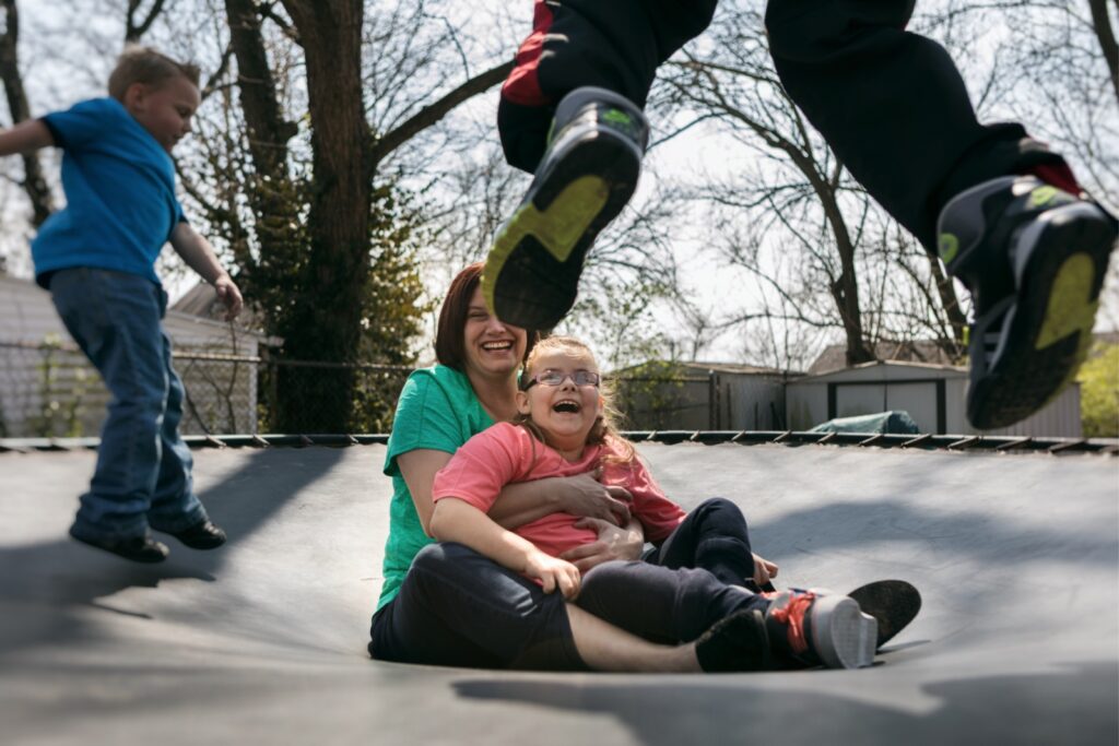 adult female foster carer holds girl on trampoline
